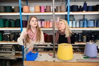 Two students with spools of coloured thread on shelves behind them
