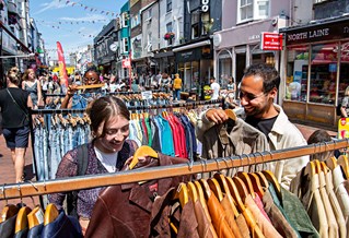 Two students in Brighton lanes conversing near a clothing rail on a sunny day