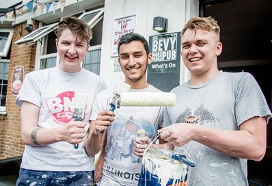 Three student volunteers with paintbrushes outside the Bevy community pub