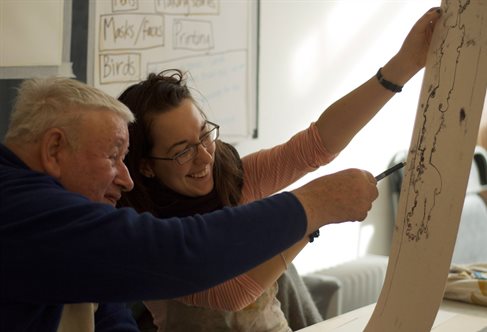 Arts practitioner Sarah Gladden holds up a paper for drawing project with elderly, vision-impaired Peter Cutts as part of an inclusive arts project.