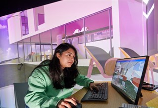 Student working on a computer with the image projected on a large screen behind her
