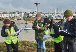 four students at a harbour with clipboards and field surveying equipment