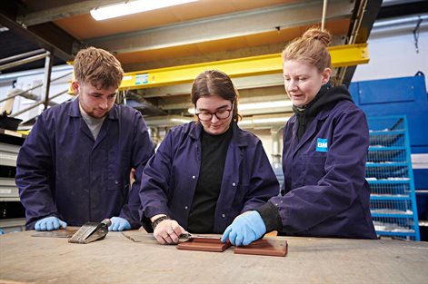 Two students on placement working with a colleague measuring tile samples in a workshop