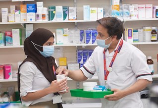 Male and female standing in front of shelf with medicines