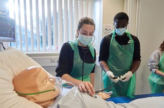 Two pharmacy students using stethoscope on patient simulation dummy
