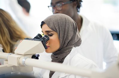 A student in a white coat looking into a microscope