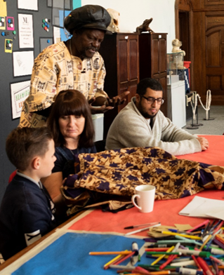 A mixed age group in a museum setting share stories of black and ethnic minority origins using cloth and textile props and writing materials