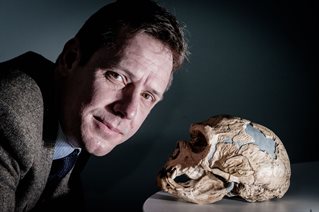 Academic in tweed jacket leans over a reconstructed skull of a prehistoric ancestor. Dr James Cole researching early human canibalism.