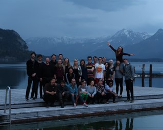Group of young people stand for camera on a low pier with mountains in background. Climate communications retreat, St Gilgen Austria