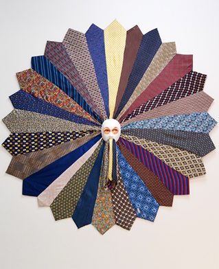 Wall mounted artwork by Susan Diab. Tie tongued is created with a radiating circle of ties with a mask face in the middle.