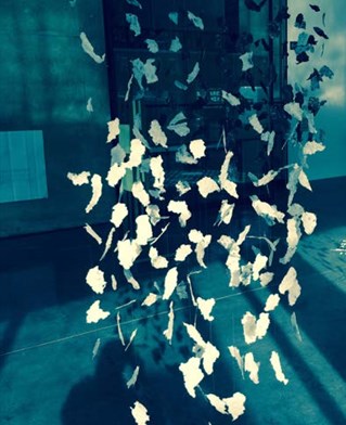 Blue lit photograph of installation space with hanging paper fragments. Artist Jules Findley explores grief.
