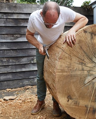 Photograph of wood craftsman Gareth Neal hand carving a giant wheel from a cross section of an elm trunk.