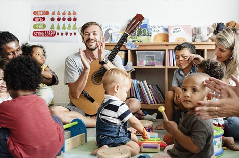male teacher playing guitar at a toddler group