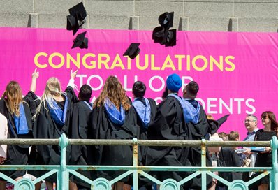 A group of graduates on the seafront promenade throwing their mortar boards in the air