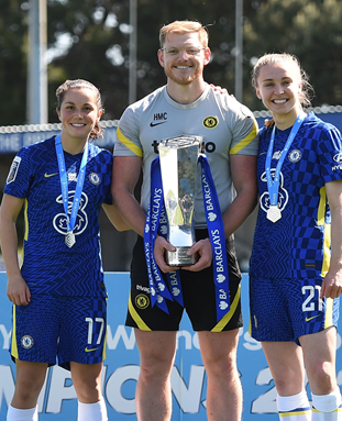 Harry McCulcoh holding a trophy with two members of Chelsea FC Women