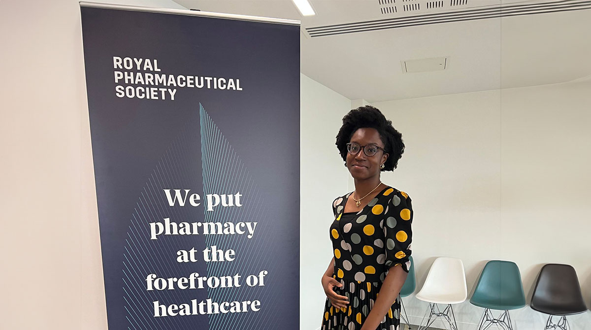 Photography of a black woman standing next to a banner about pharmacy health care
