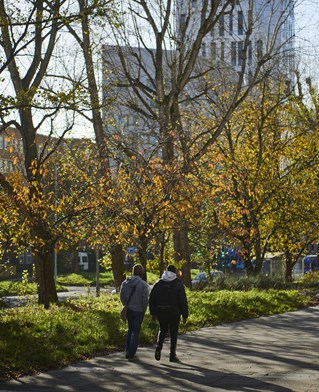 Two students walking past some trees with Mithras Halls in the background