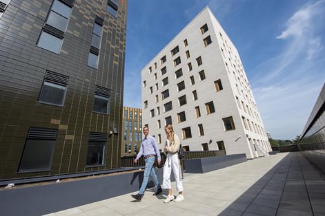 Lecturer (left) and student (right) walking in front of Mithras halls of residence