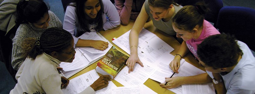 Students sitting around desk pointing to documents 