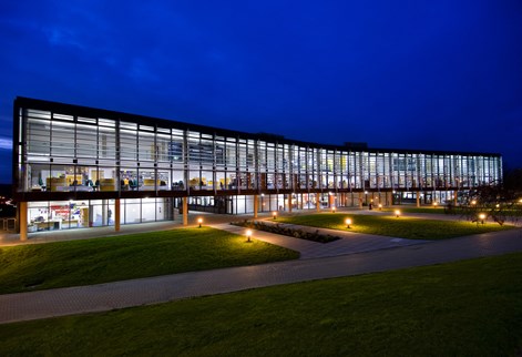 Night view of the long, low glass Checkland Building, University of Brighton, lit from interior.