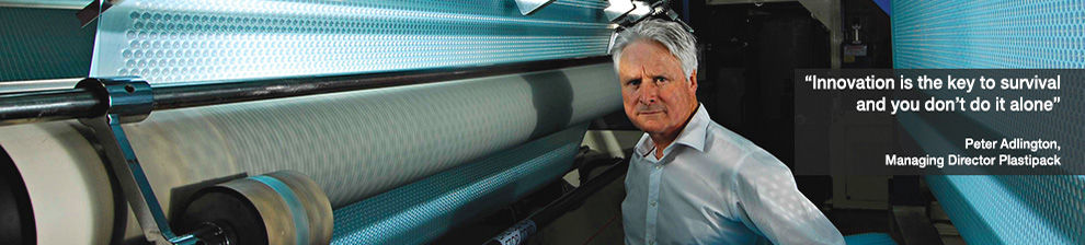 Managing Director of Plastipak stadning between rolls of blue plastic