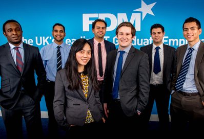 Seven people in business attire standing in front of the FDM logo