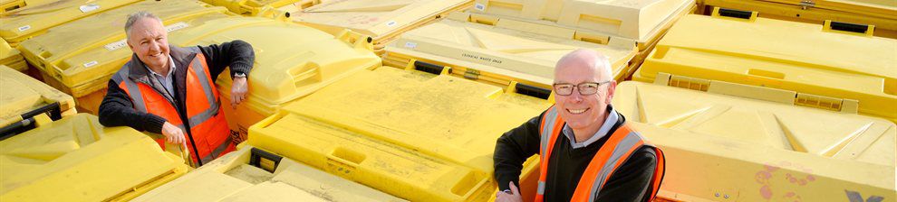 Two people in hi-viz surrounded by large yellow bins