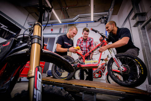 Three people working on a bicycle in a workshop
