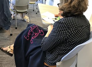 A photograph of a woman with 'Everyday Creativity embroidered on a piece of material in her lap