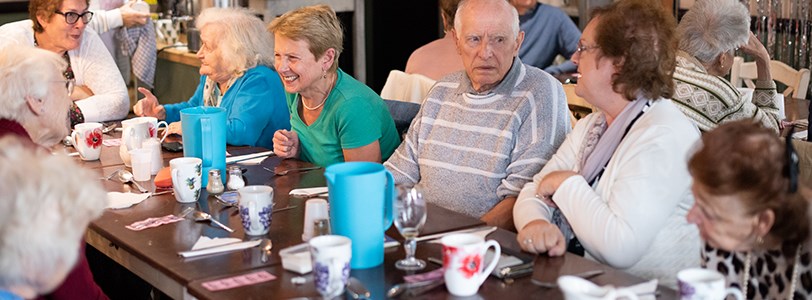 Group of elderly people at a long table enjoying tea and cakes as part of the University of Brighton's living lab