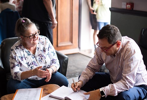 Two people around a table, one writing