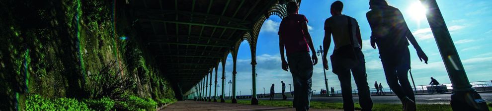 University students silhouetted against blue sky under promenade arches on Brighton Seafront