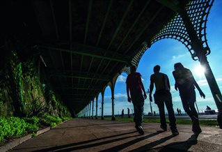 Research students silhouetted against blue sky under promenade arches on Brighton seafront