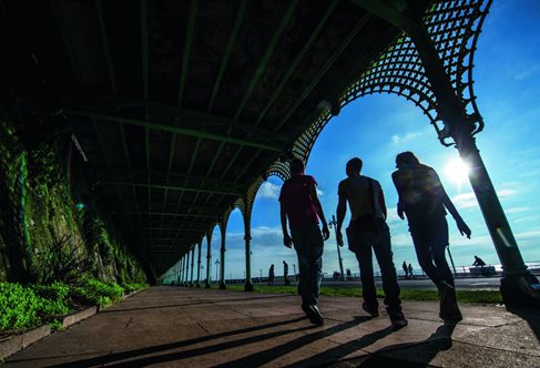 Silhouette of three students under arches against blue sky on Brighton seafront