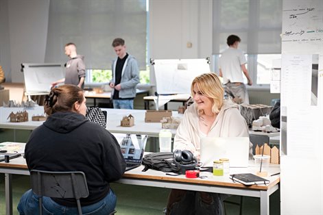 Two students talking across a desk in an architecture studio