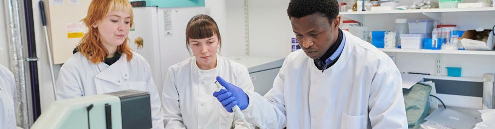 Three PG students working in lab with bottles wearing white lab coats