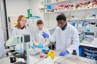 Three PG students working in lab with bottles wearing white lab coats