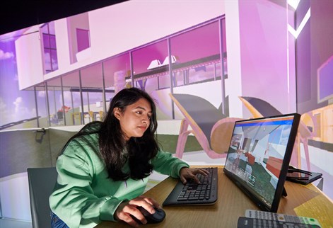 Student working on a computer with large projection of a building behind her