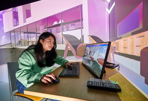 Student working on a computer with large projection of a building behind her
