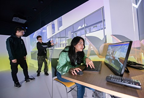 Female in front of computer with two students in immersive learning space