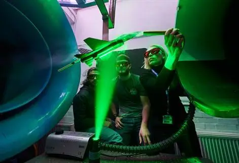 Lecturer demonstrating wind tunnel to two students wearing goggles with lazer green light