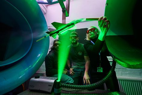 Lecturer demonstrating wind tunnel to two students wearing goggles with lazer green light