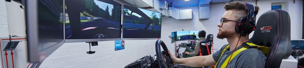 Student using an engineering driving simulator looking at three screens with graphics