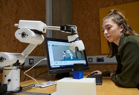 Student with long hair in front of computer working a robot arm