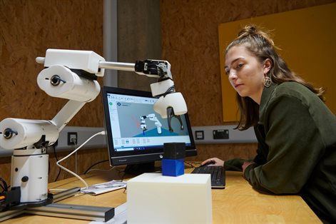 Student with long hair in front of computer working a robot arm