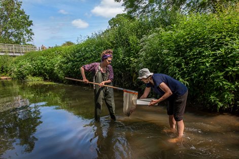 Female student and female lecturer with net collecting samples from river
