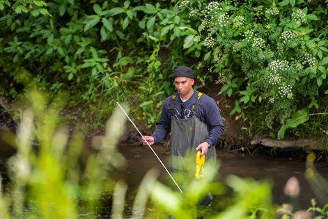 Male student standing in river collecting samples