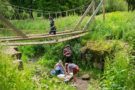 One female walking over a rope bridge with three students underneath it looking at samples