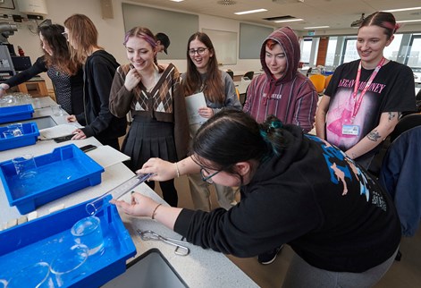 Group of students watching one person our liquid between two glass containers in a geography lab