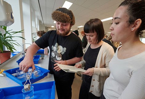 Lecturer with two students one putting a small block into a container of liquid